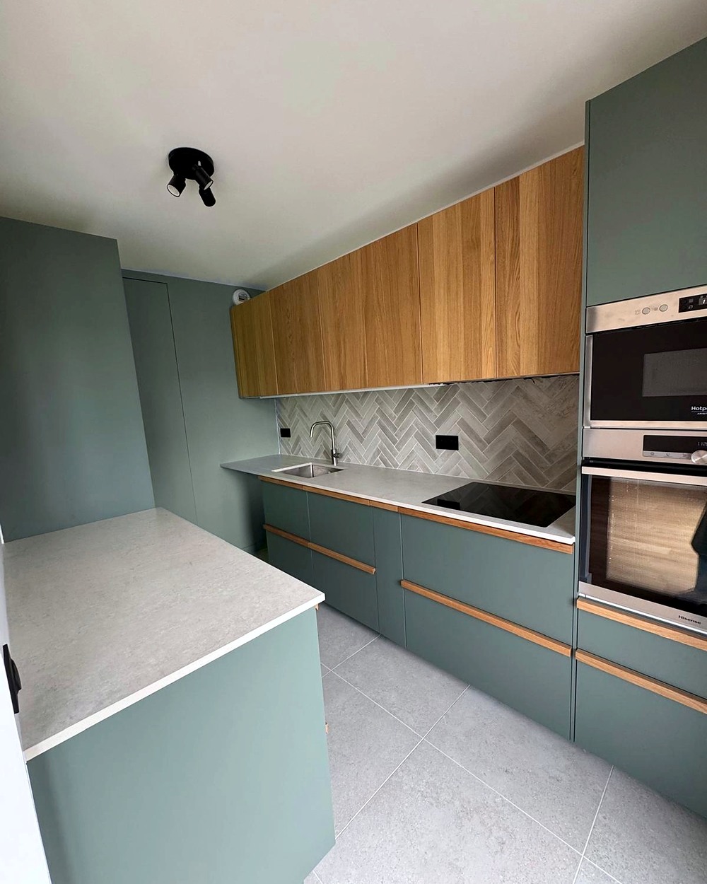Cuisine sur mesure aux façades vert de gris et chêne, crédence en chevrons